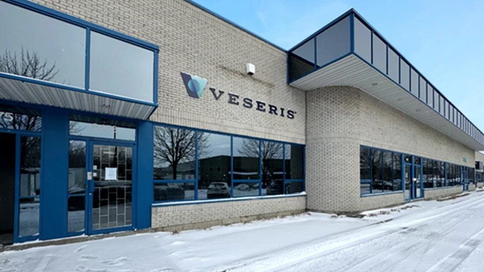 A tan brick building with glass windows and blue framing. A sign with black text reads Veseris.