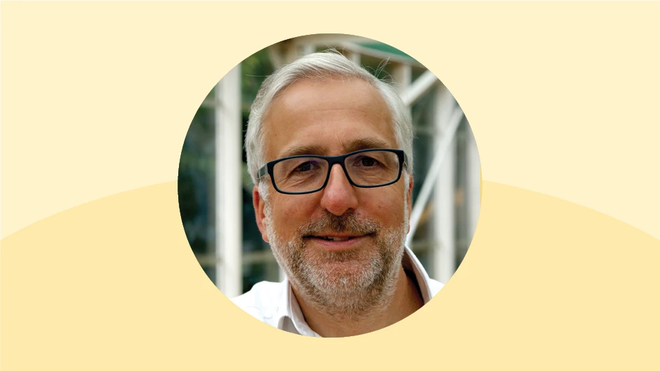 A photo of a smiling man with short white hair and short gray facial hair wearing black glasses.